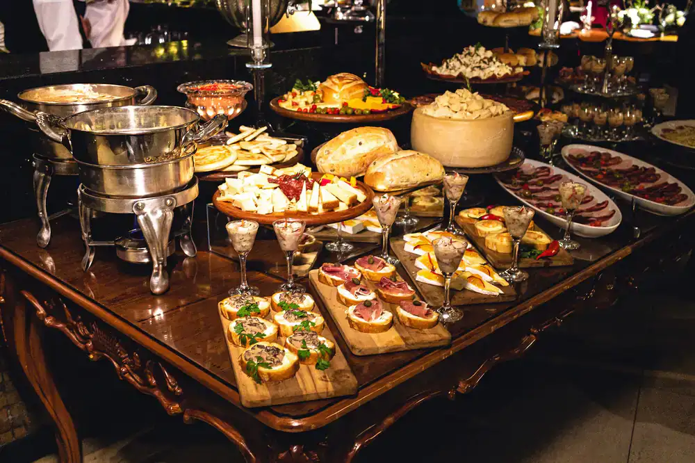 A large wooden table filled with assorted cheeses, cured meats, and fresh fruits