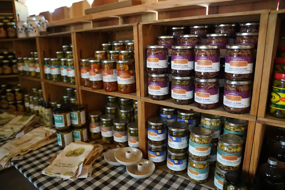 Jars of chutneys, honeys, and pickled vegetables on wooden shelves